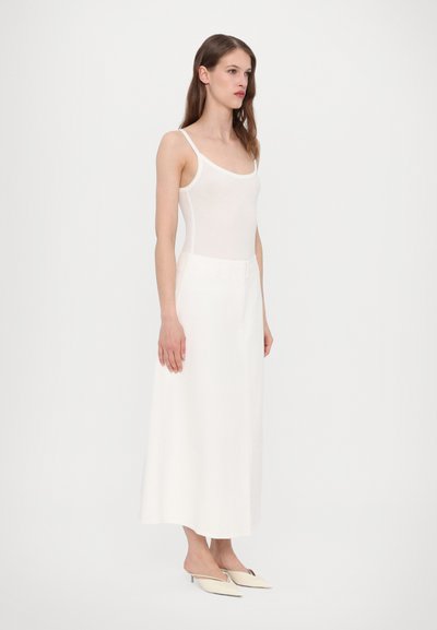 Hvid tætsiddende tanktop parret med en lang hvid nederdel; glat tekstur, minimalistisk design, med et taljebælte og spidse slip-on hæle.