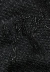 Tessuto in denim nero con cuciture goffrate sottili e un design ondulato, che mette in risalto la texture e la profondità del materiale.