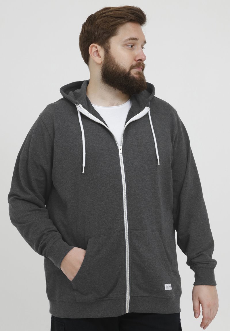 Sudadera gris con cremallera hecha de tejido suave, con una cremallera frontal, cordones blancos y dos bolsillos laterales. Corte clásico con un diseño casual.