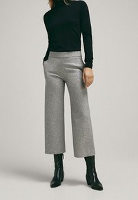 Pantaloni larghi grigi con una texture liscia, vita alta e tasche laterali, abbinati a un dolcevita aderente nero e stivali neri alla caviglia.