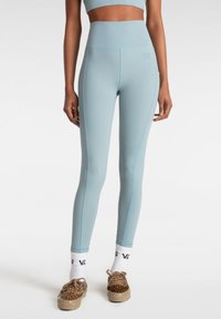 Leggings a vita alta di colore azzurro realizzati in tessuto elastico, con cuciture di un blu chiaro a contrasto e una cintura testurizzata. Senza logo visibile.