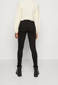 Svarta jeans med smal passform, tillsammans med en krämfärgad stickad tröja med texturerad tyg och långa ärmar. Svarta ankelstövlar fullända looken.