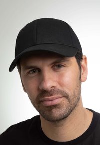 Cappellino da baseball nero con un design strutturato, tessuto liscio, visiera curva e cuciture visibili. Indossato da un uomo con capelli corti e barba incolta.