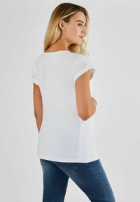 T-shirt bianco a maniche corte con risvolti, caratterizzato da una vestibilità comoda e una texture liscia, abbinato a jeans blu aderenti.