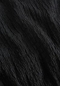 Gros plan sur un tissu noir montrant une surface texturée et froissée en détail, avec des ombres subtiles mettant en valeur le motif en relief.