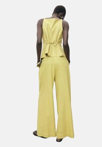 Conjunto de dos piezas a rayas amarillas que incluye un top peplum con lazo y pantalones de pierna ancha. La tela parece ligera y tiene un acabado texturizado.