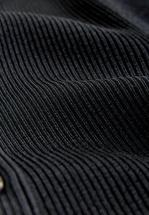 Nahaufnahme von schwarzem geripptem Cordstoff, der strukturierte vertikale Rillen und weiche Falten zeigt.