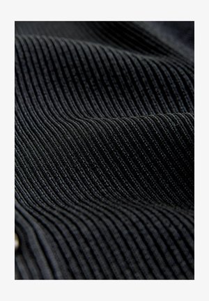 Nahaufnahme von schwarzem geripptem Cordstoff, der strukturierte vertikale Rillen und weiche Falten zeigt.