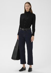 Fekete, gombos ing puha anyagból, sötétkék, bőszárú farmerral, fekete bőr övvel és fekete bebújós cipővel párosítva.