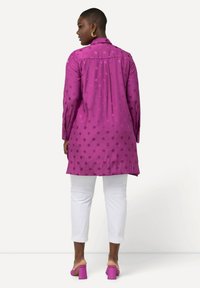 Chemise à manches longues, violette avec un motif circulaire, dotée d'un pli au dos. Associée à un pantalon blanc cropped et des sandales à talons carrés roses.
