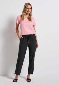 Ljusrosa kortärmad t-shirt som kombineras med svarta, löst sittande byxor med dragsko i midjan och två framfickor. Platta svarta sandaler.