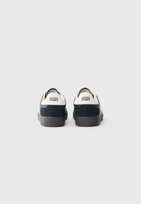 Un paio di sneaker Jack & Jones navy e bianche viste da dietro, con suole nere su uno sfondo bianco.