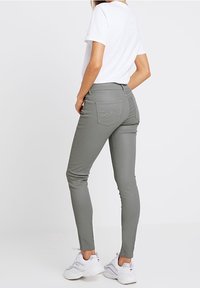 Úzké šedé džíny vyrobené z pružného materiálu, s středně vysokým pasem a zadními kapsami se decentními švy. V kombinaci s bílým tričkem.