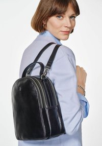 Czarny skórzany plecak z podwójnymi komorami na zamek błyskawiczny, o zakrzywionym kształcie i regulowanymi szelki. Gładka tekstura o minimalistycznym wzornictwie.