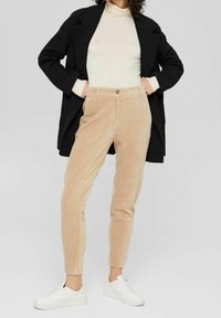 Beige kordflorsbyxor med slim fit, med knäppning, sidofickor och ribbad textur, ihop med en åtsittande topp och svart kappa.