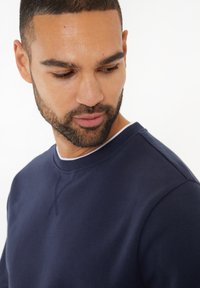 Granatowa bawełniana bluza z okrągłym dekoltem, charakteryzująca się fakturowanym wykończeniem oraz subtelnymi detalami w postaci przeszyć wzdłuż kołnierza i szwów na ramionach.