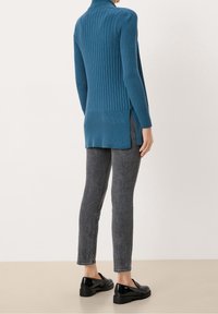 Blå ribbad tröja med hög hals, långa ärmar, sidokilar, parat med grå smala jeans och svarta glansiga skor. Slät textur.