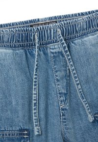 Shorts de mezclilla con cintura elástica, cierre de cordón, color azul claro y bolsillo frontal con detalles de costura.