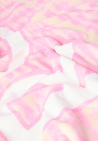 Mäkká, nadýchaná prikrývka s geometrickým vzorom v ružovej a krémovej farbe na bielom podklade, s hladkým, textúrovaným povrchom.