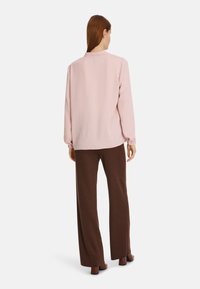 Helles rosa Langarmoberteil mit lockerer Passform, elastischen Manschetten und abgerundetem Saum, kombiniert mit braunen weiten Hosen. Glatte Textur über das gesamte Kleidungsstück.