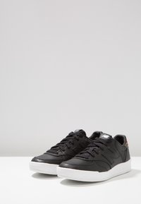 Baskets en cuir noir avec semelles en caoutchouc blanc, dotées de lacets noirs et d'un logo sur la languette. Accent arc-en-ciel remarquable sur le talon.