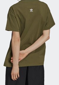 Olivgrön bomullströja med kort ärm, avslappnad passform och liten vit Adidas-logotyp på ryggen. Slät yta, enkel design.