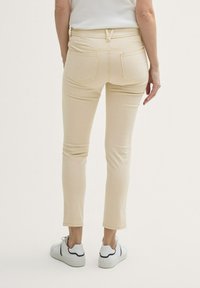Beige skinny jeans met achterzakken, een mid-rise taille en subtiele stikdetails. Gepaard met witte sneakers.