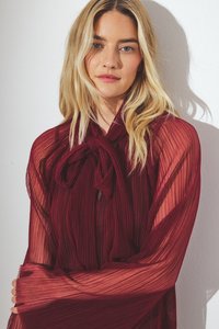 Bordeauxfarbene plissierte Bluse mit Krawattenkragen und durchsichtigen Ärmeln, aus einem strukturierten Stoff mit fließendem Design. Glatte Oberfläche mit sanftem Fall.