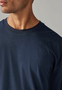Tumed ümmarguse kaelusega T-särk, mis on valmistatud pehmest kangast, millel on sile tekstuur ja lühikesed varrukad, ilma nähtavate mustrite või logodeta.