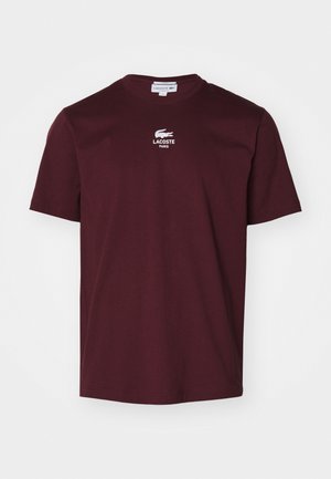 T-shirt de algodão burgundy com gola redonda, mangas curtas e logotipo bordado branco da Lacoste com a inscrição "LACOSTE PARIS". Textura suave, corte regular.