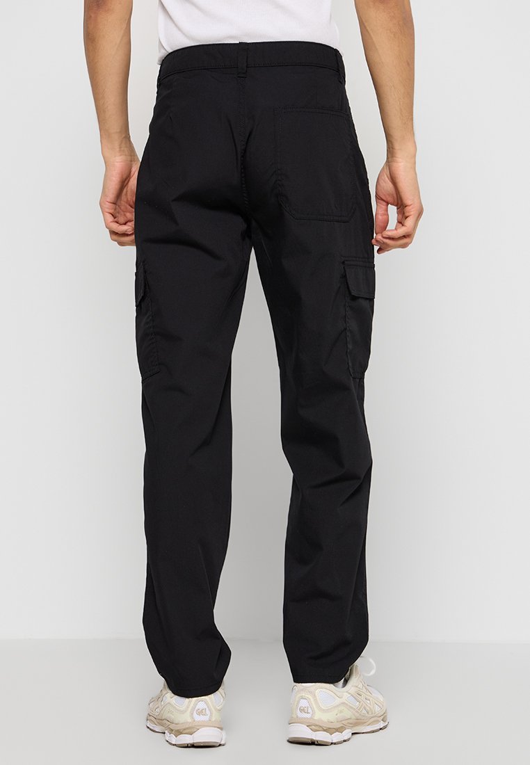 Pantalons cargo noirs à coupe décontractée, dotés de poches latérales et de poches arrière, fabriqués à partir d'un tissu durable. Portés avec des baskets de couleur claire.