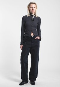 Harmaa ribattu pitkähihaisuus ykkönen, jossa on napit, yhdistettynä löysiin mustiin farkkuihin. Mustat kengät, joissa on hienovaraisia ompelutuksia.