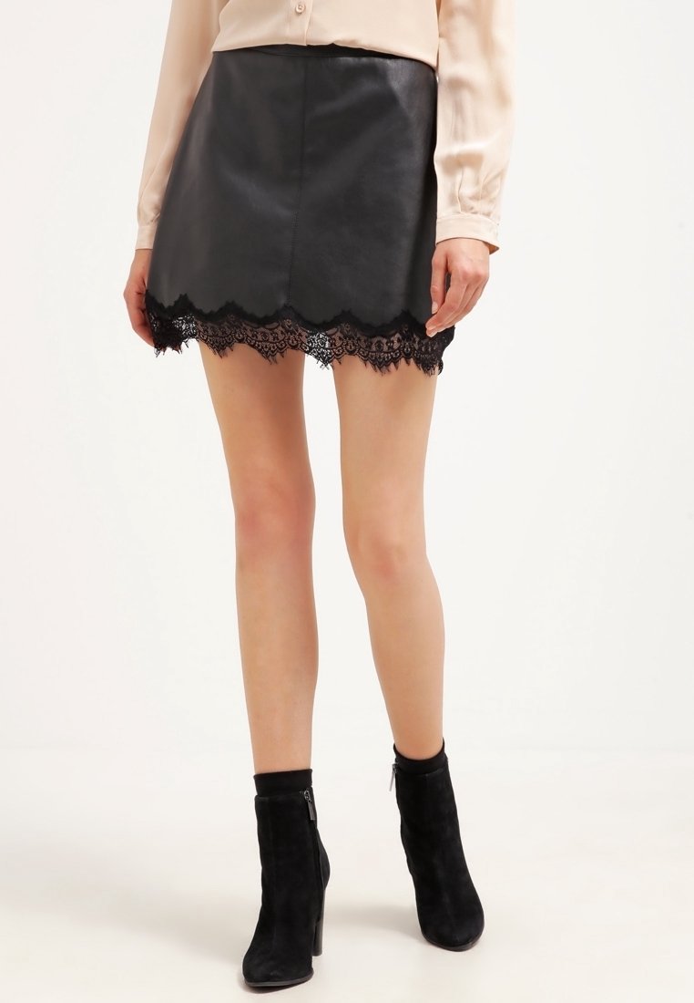 Mini-jupe en cuir noir avec un ourlet en dentelle noire délicate. Présente une texture lisse et une coupe ajustée. Portée avec des bottines noires.