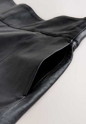 Sort læderbeklædning med en glat tekstur, udstyret med en åben lomme og pæn syning langs kanterne. Subtil glans fremhæver materialet.