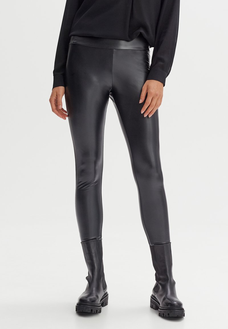 Leggings in ecopelle nera con un design aderente, una texture liscia e un'alta vita, abbinati a stivali neri con tacco chunky.