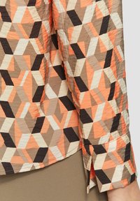 Geometrisch patroon shirt in perzik-, bruin- en crèmekleuren; heeft een textuurstof en manchet details met zwarte accenten.