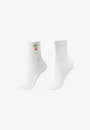 Paire de chaussettes blanches côtelées montantes avec une petite broderie de cerise rouge et de tige verte près du haut sur une chaussette.