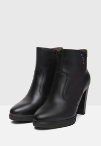 Bottes noires en cuir à hauteur de cheville avec une texture lisse, un bout pointu et un haut talon carré. Dotées d'une fermeture éclair sur le côté et de détails métalliques discrets.