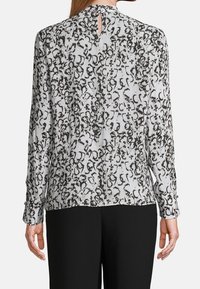 Long-sleeve blouse in light gray with black abstract pattern, featuring a keyhole cutout at the back and buttoned cuffs. Smooth texture.