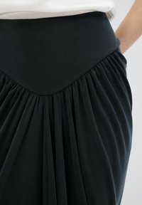 Černá sukně s širokým elastickým pasem a plisovaným designem. Měkká, hladká textura, zdůrazňující plynulost a pohyb.