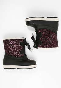 Zimowe buty dziecięce z czarnymi gumowymi podeszwami i górną częścią w purpurowym kolorze z brokatem, wyposażone w czarne zapięcia na sznurki i białe futerko wewnątrz.