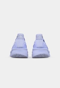 Ett par ljuslila Adidas-sneakers visade från baksidan, vilket framhäver den tjocka sulan och logotypen på hällappen mot en vit bakgrund.