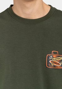 Olivengroene sweatshirt met een ronde halslijn en een grafische logopatch met een ontwerp van een oranje koffer. Zachte stof, casual pasvorm.