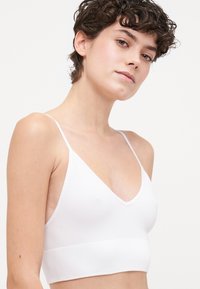 Bralette blanc côtelé avec des bretelles spaghetti ajustables et une large bande. Décolleté en V et texture douce, idéale pour le superposition ou un style décontracté.