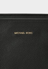 Zwart leren portemonnee met een gestructureerde oppervlakte. Voorzien van gouden "MICHAEL KORS" branding. Compacte rechthoekige vorm. Randstiksel zichtbaar.