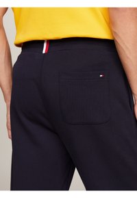 Marineblaue Baumwollhosen mit einer Gesäßtasche, die mit einem kleinen rot-weißen-blauen Logo akzentuiert ist. Glatte Textur, lässiges Design.