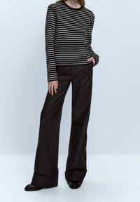 Camicia a maniche lunghe a righe in bianco e nero, abbinata a pantaloni larghi scuri. La camicia ha un col rotondo; i pantaloni presentano una texture liscia.