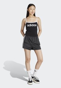 Černý tílko s bílým logem "adidas", doplněné černými pruhovanými šortkami s bílými bočními pruhy a logem. Černobílé boty dokončují vzhled.