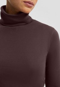 Bordowy golf wykonany z gładkiej, elastycznej tkaniny. Posiada długie rękawy i dopasowany fason. Brak widocznych wzorów i ozdób.