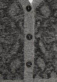 Grijze cardigan met een textuur, gebreid ontwerp. Voorzien van een zwarte knoopsluiting en een subtiel patroon dat metalen draden verwerkt.